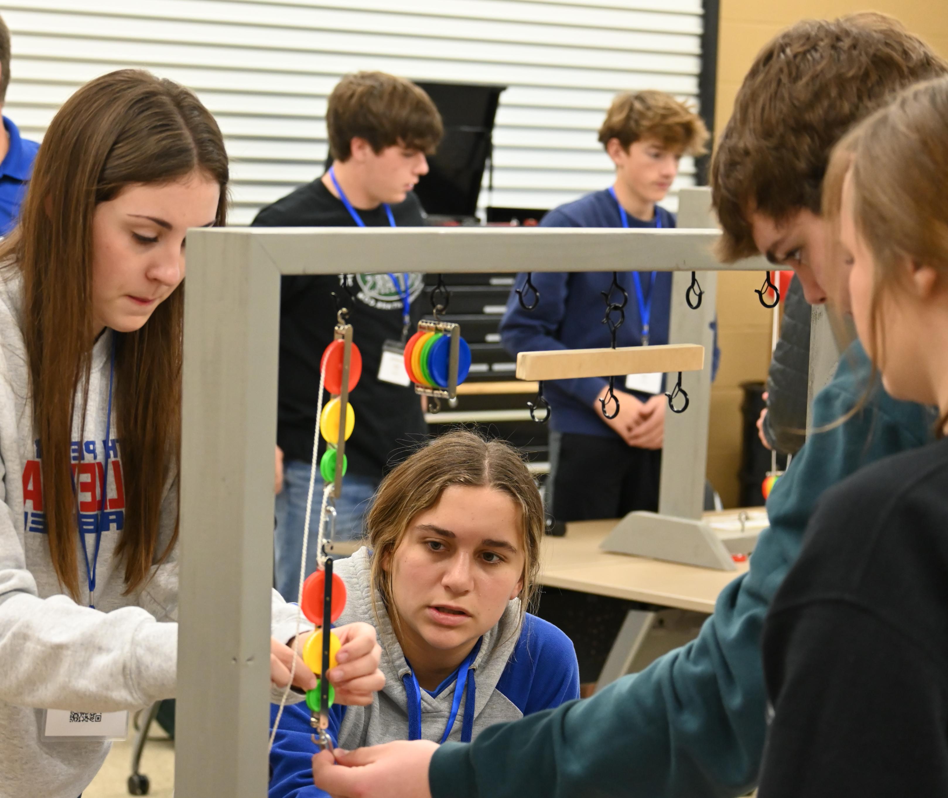 Female and male high school students competing in a CTIM Challenge with mulitcolored pulleys in a classroom.